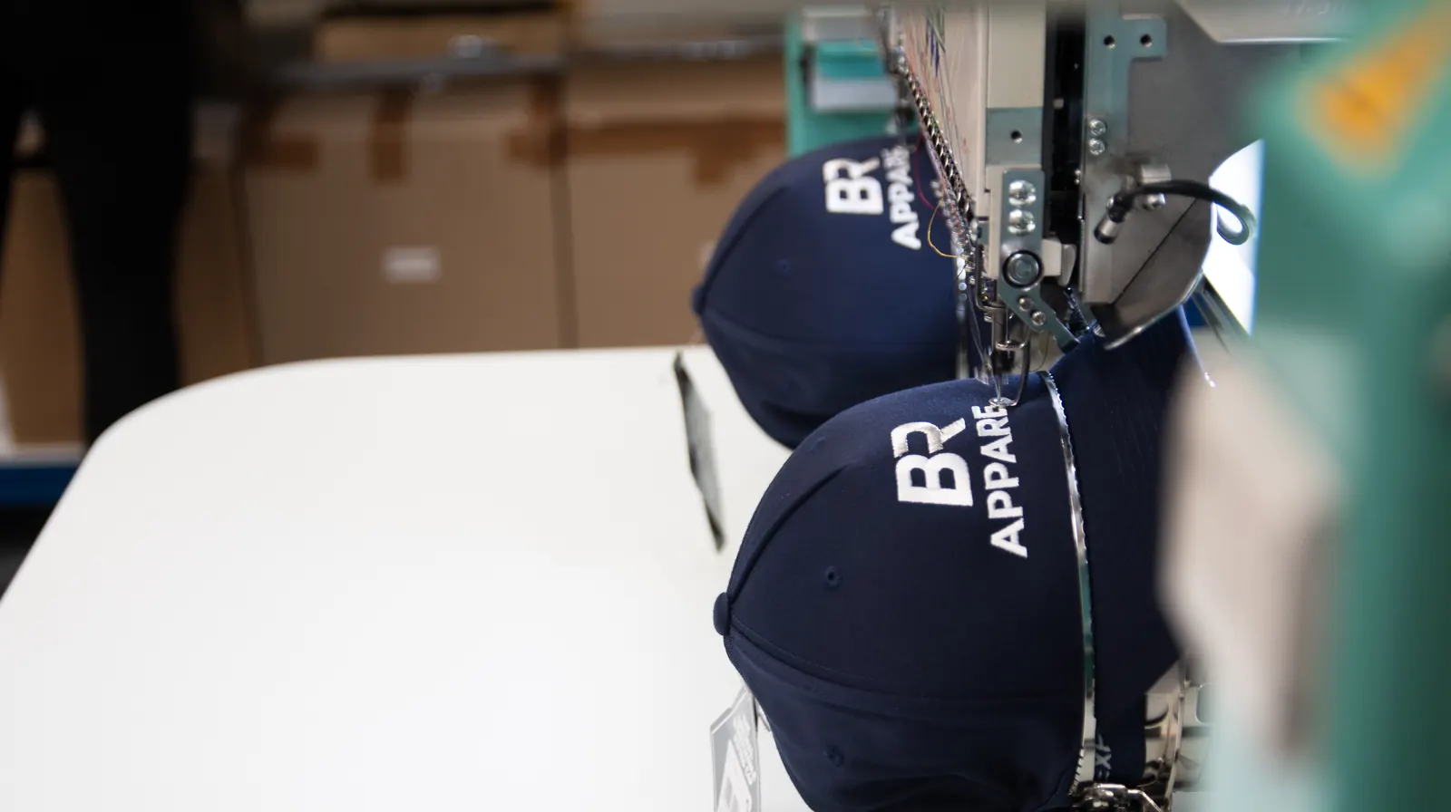 Close-up of embroidery machine stitching branded logos onto caps