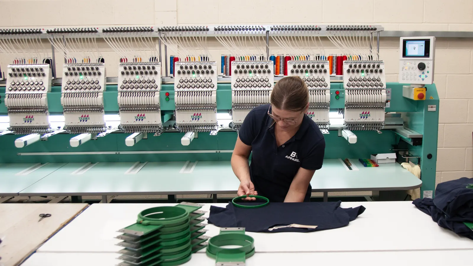 Multi-head Tajima embroidery machine running a batch of navy garments
