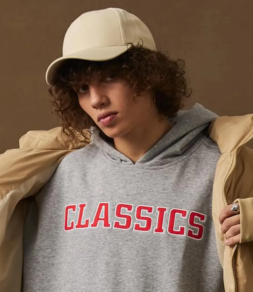 Model in a grey hooded sweatshirt wearing a plain stone curved peak cap