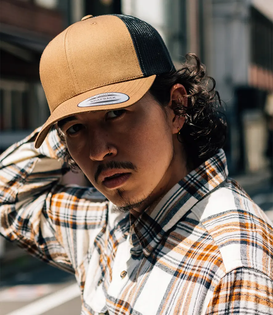 Model wearing a two tone trucker cap with a camel front panel and a black mesh back